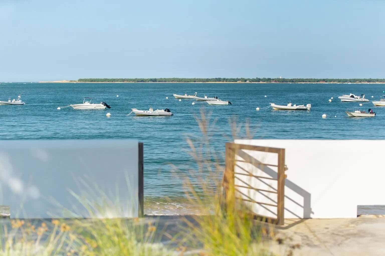 Vue sur le Bassin d'Arcachon depuis un ponton, bateaux amarrés et dune du Pilat au loin