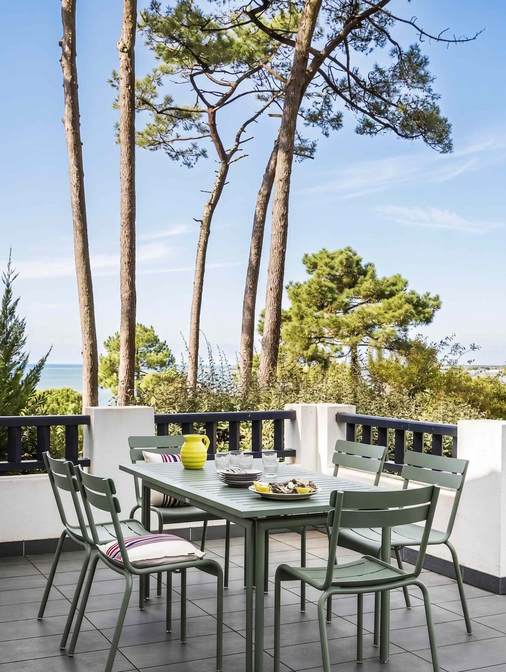 Terrasse repas en métal vert, pins maritimes et aperçu de la mer en arrière-plan