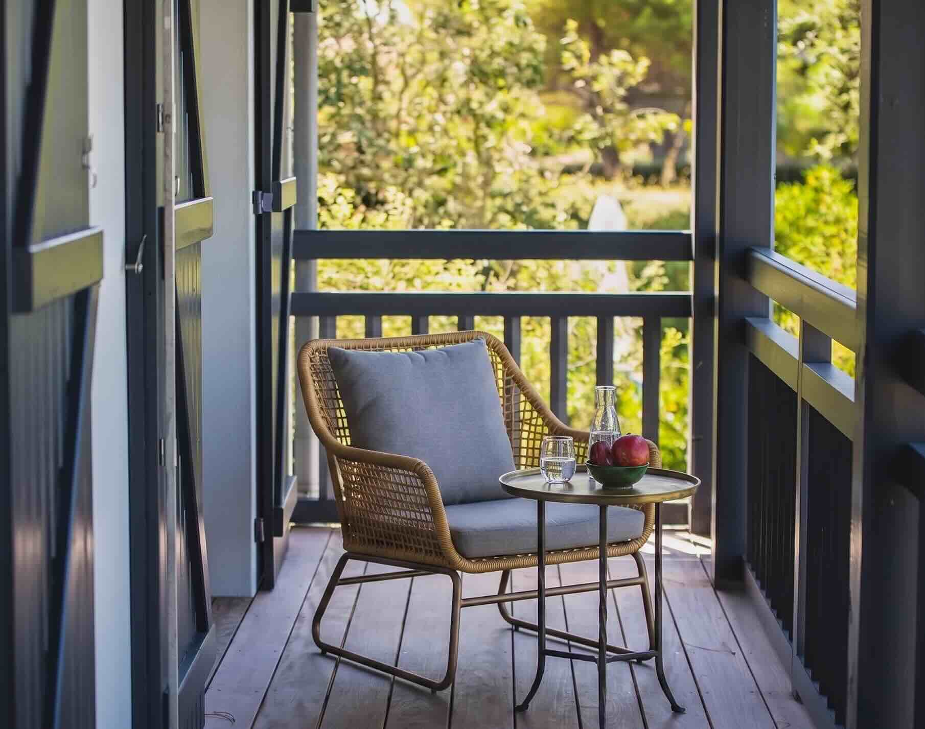 Fauteuil en rotin sur une terrasse en bois, vue sur jardin ombragé